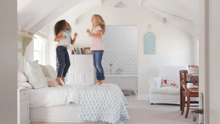 Two girls jumping on a bed in a bright bedroom